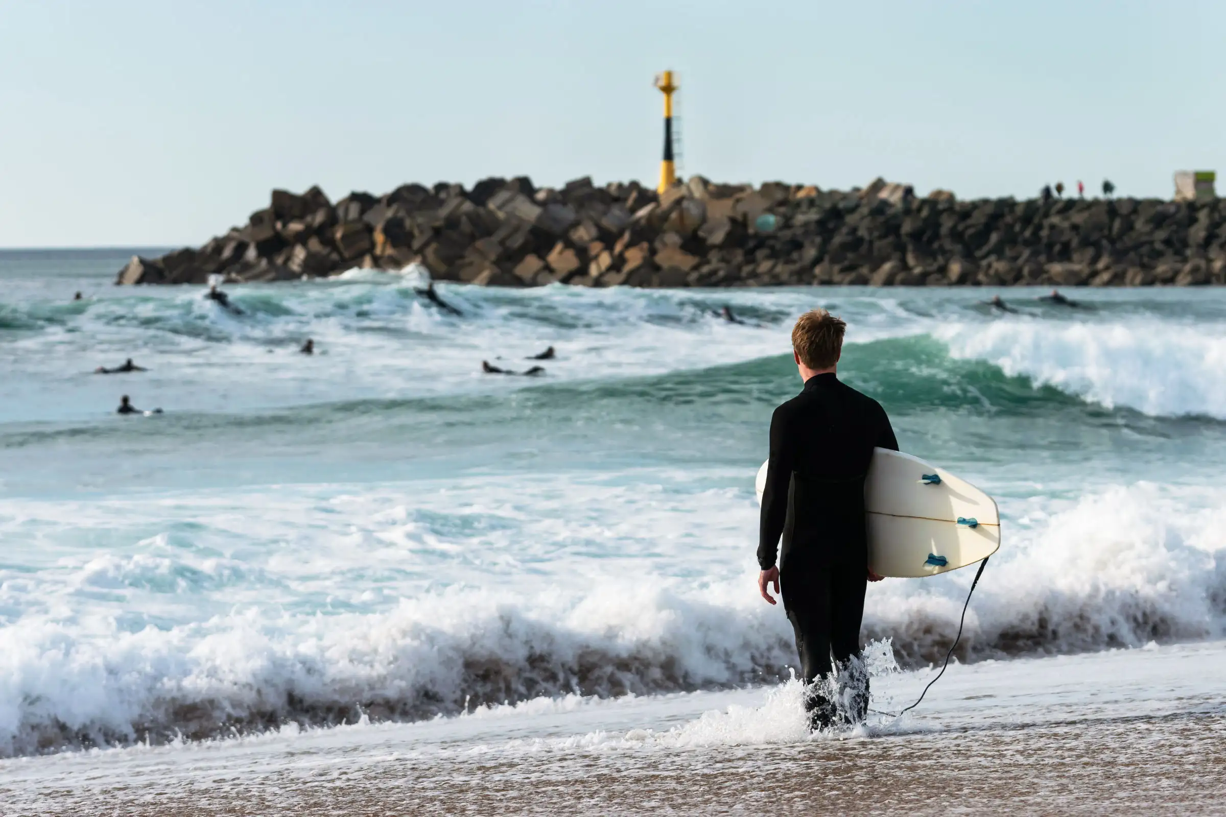 Surfer holding his board, facing the ocean near the jetty at Les Cavaliers beach in Anglet, on the Basque coast