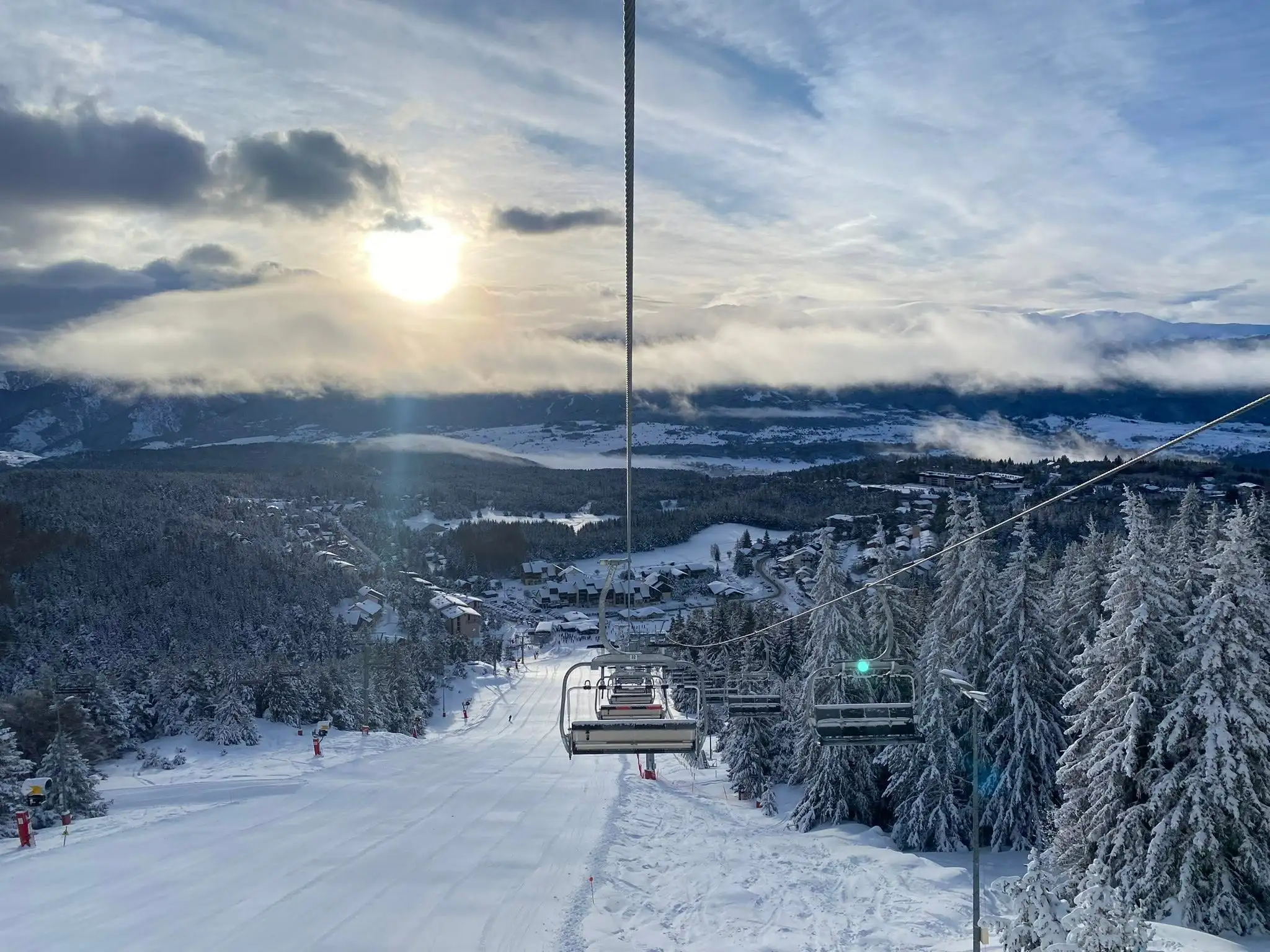 View from a chairlift overlooking a snow-covered ski slope and a forest of fir trees, likely at the Font-Romeu Pyrénées 2000 ski resort